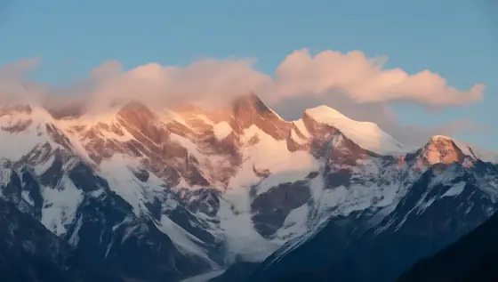 这张令人惊叹的喜马拉雅山照片，其白雪皑皑的山峰在阳光的照耀下，营造出令人着迷和敬畏的场景。天空是清澈的蓝色，柔和的粉红色和橙色云彩为其增添了美感。这张照片捕捉到了这些山脉的雄伟自然，唤起了人们的惊叹和壮丽景色。